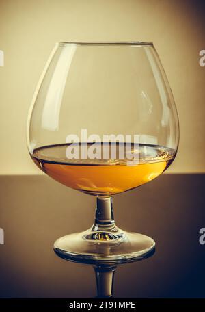 Schnitzel von Brandy in elegantem, typischem Cognacglas auf altmodischem Hintergrund, mit Reflexion Stockfoto