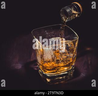 Barkeeper, der Whiskey ins Glas auf Holztisch gießt, warme Atmosphäre, alter westlicher Stil, Zeit der Entspannung mit Whisky mit Platz für Text Stockfoto
