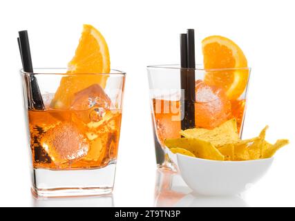 aperol-Cocktail mit Orangenscheiben und Eiswürfeln in der Nähe von Tacos-Chips auf weißem Tischhintergrund Stockfoto