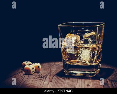 würfel in der Nähe von Whiskey Glas auf alten Holztisch, Konzept des Spiels Entspannen Sie Zeit mit Whisky Stockfoto