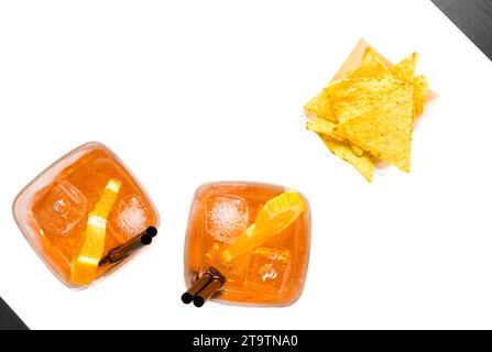 Blick von oben auf heiße Tacos Chips in der Nähe von zwei Gläsern Spritz aperol Cocktail mit Orangenscheiben und Eiswürfeln auf weißem Tisch Stockfoto