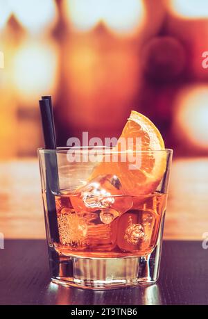 Ein Glas Spritz-aperol-Cocktail mit Orangenscheiben und Eiswürfeln auf dem Bartisch, Vintage-Atmosphäre im Hintergrund, Lounge-Bar-Konzept Stockfoto