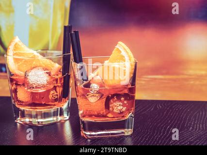 aperol-Cocktail mit Orangenscheiben und Eiswürfeln auf dem Bartisch, Vintage-Atmosphäre im Hintergrund, Lounge-Bar-Konzept Stockfoto