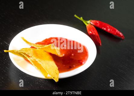 Knusprige Maisnachos mit scharfer Tomatensauce als Snack oder Vorspeise in einer weißen Scheibe auf schwarzem Holztisch Stockfoto