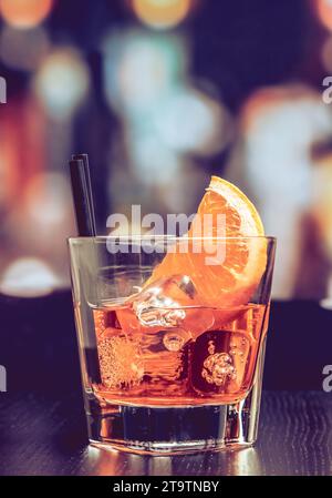 Ein Glas Spritz-aperol-Cocktail mit Orangenscheiben und Eiswürfeln auf dem Bartisch, Vintage-Atmosphäre im Hintergrund, Lounge-Bar-Konzept Stockfoto