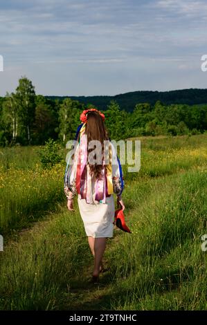 Das Mädchen, mit dem Rücken gewendet und in ukrainischer Nationalkleidung gekleidet, läuft barfuß auf dem Feld, trägt einen Kranz mit Bändern auf dem Kopf. Stockfoto