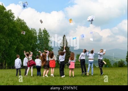 Eine Gruppe junger Schüler wirft ihre Notizbücher hoch, Berge und Wald im Hintergrund. Stockfoto