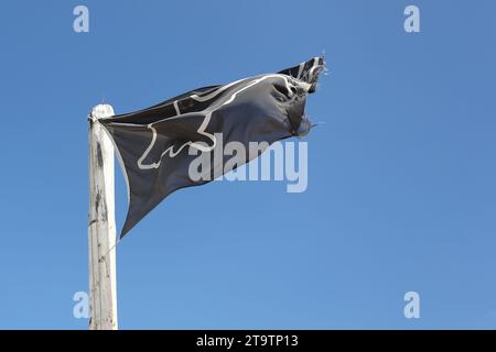 Eine allgemeine Ansicht einer Warnflagge für Schwarze Haie vor blauem Himmel am Muizenberg Beach in Kapstadt, Südafrika. Eine schwarze Flagge mit weißem SHA Stockfoto