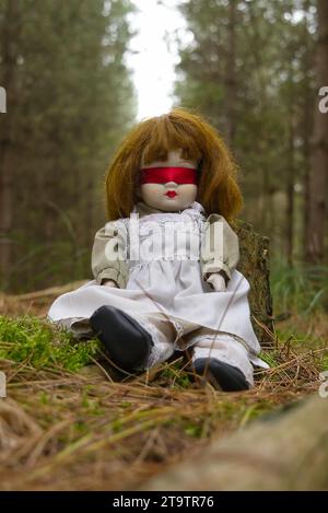 Gruselige Puppe mit roter Schleife, im Wald verlassen. Thriller, Horror. Stockfoto