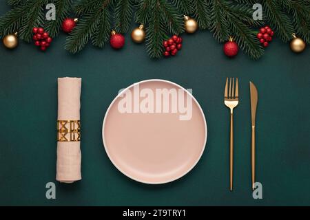 Weihnachtstisch mit Dekoration. Leere Platte, Gabel, Messer. Goldenes Besteck, dunkelgrüner Hintergrund. Draufsicht. Festplatz, immergrüner Baum. Stockfoto