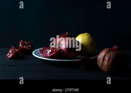 Frische Granatäpfel auf alten rustikalen Tisch Stillleben in dunklen Tönen. Reife und saftige Granatapfelfrüchte in Nahaufnahme auf schwarzem Hintergrund. Stockfoto