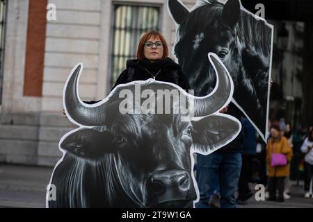 Madrid, Spanien. November 2023. Ein Anti-Stierkampf-Aktivist steht bei einem Protest vor dem Präsidentengebäude der Gemeinschaft Madrid unter den Papptierköpfen. Aktivisten des Internationalen Anti-Stierkampf-Netzwerks mit riesigen Stier- und Pferdeköpfen führen im Zentrum von Madrid eine Protestaktion für die Abschaffung des Stierkampfes durch. Quelle: SOPA Images Limited/Alamy Live News Stockfoto