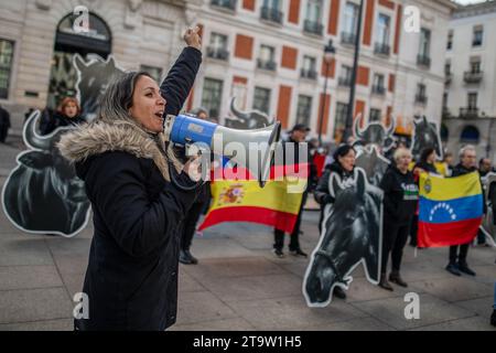 Madrid, Spanien. November 2023. Eine Aktivistin hebt ihre Faust und spricht Demonstranten während eines Protestes vor dem Präsidentengebäude der Gemeinschaft Madrid mit einem Megaphon an. Aktivisten des Internationalen Anti-Stierkampf-Netzwerks mit riesigen Stier- und Pferdeköpfen führen im Zentrum von Madrid eine Protestaktion für die Abschaffung des Stierkampfes durch. Quelle: SOPA Images Limited/Alamy Live News Stockfoto