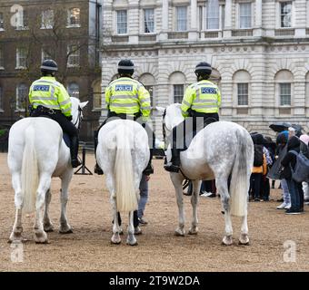 Ein Trio berittener Metropolitan Polizisten neben einer Gruppe von Touristen, die an einem regnerischen Tag Rettungsschwimmer-Soldaten bei der Parade der Horse Guards beobachten. Stockfoto