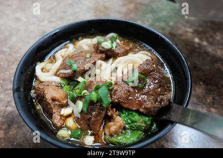 Rindfleischnudeln Chilisauce serviert in einer Schüssel auf dem Tisch mit Blick auf taiwanesische Speisen. Suppe Rindernudeln in einer Schüssel auf Holztisch. Chinesische taiwanesische Küche Stockfoto