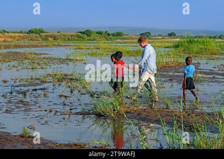 Madagassische Kinder helfen Westtouristen durch die Auen entlang des Tsiribihina River in der Nähe von Ambotomisay, Menabe, Central Highlands, Madagaskar, Afrika Stockfoto