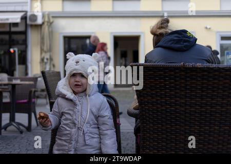 Belgrad, Serbien, 19. November 2023: Ein kleines Mädchen mit französischem Gebäck steht neben ihrer Mutter, die Kaffee in einem Café im Freien genießt Stockfoto