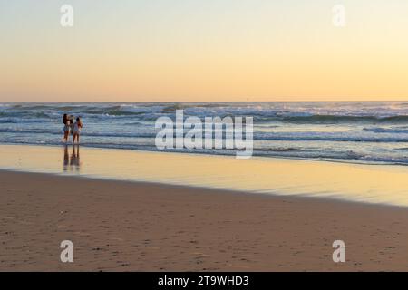 Surfers Paradise Australia - 21. September 2023; drei junge Frauen stehen bei Sonnenaufgang im seichten Wasser und machen Handyfotos. Stockfoto