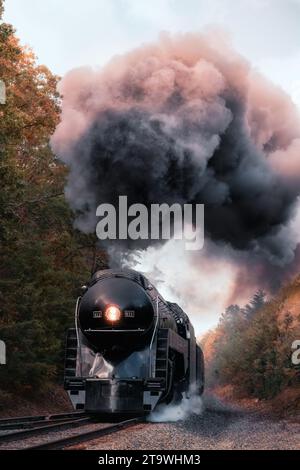 Eine alte Dampflokomotive, die eine Wolke aus grauem Rauch ausstrahlt, während sie die Gleise entlang zieht Stockfoto