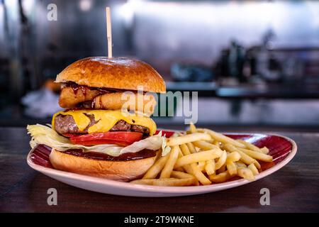 Ein frisch gegrillter Rindfleisch-Cheeseburger gefüllt mit Zwiebelringen und serviert mit Pommes frites. Stockfoto