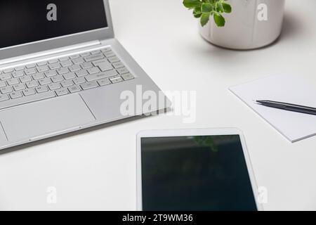 Schreibtisch mit Laptop, Tablet, Notebook und Blume in einem weißen Topf im Hintergrund. Stockfoto