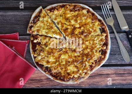 Frisch gebackene hausgemachte Pizza auf rustikalem Holztisch. Leckere Hühnchenpizza mit Käse, Pizzascheibe. Rote Serviette, Messer und Gabel. Draufsicht. Stockfoto