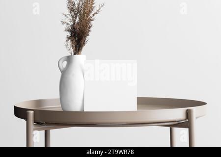 Quadratische Einladungskarte Mockup mit getrocknetem Blumenschmuck auf dem beigen Tisch. Stockfoto