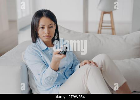 Ruhige junge Frau mit Fernbedienung, Auswahl aus verschiedenen Unterhaltungsmöglichkeiten Stockfoto