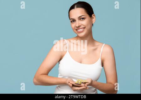 Hübsche junge Frau, die Blisterpackungen mit Vitamin-A-Kapseln auf blauem Hintergrund hält Stockfoto