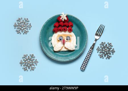 Teller mit Pfannkuchen in Form des Weihnachtsmanns auf blauem Hintergrund. Weihnachtsfeier Stockfoto