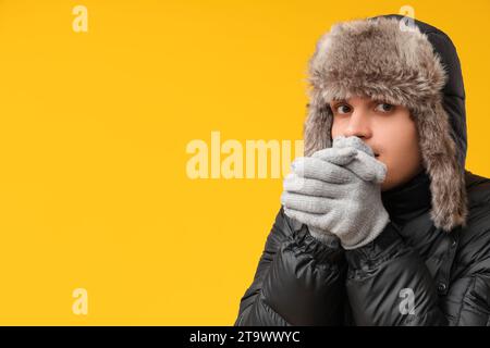 Junger Mann in schwarzer stilvoller Pufferjacke und Hut auf gelbem Hintergrund Stockfoto