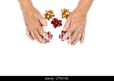 Alte faltige weibliche Hände, die einen Satz von Neonfolien-Bögen in Rot- und Goldfarben auf weißem Hintergrund halten. Frohe Feiertage. Kopierbereich. Blick von oben Stockfoto