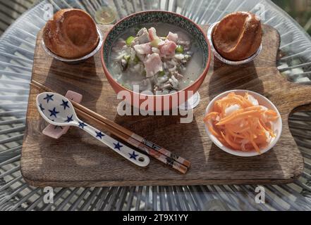 Heißer gekochter Reis oder Reisbrei mit Schweinerippchen Suppe und Schinken serviert mit frittiertem Teig, eingelegter Karotte und Rettich auf hölzernem Schneidebrett. Er Stockfoto