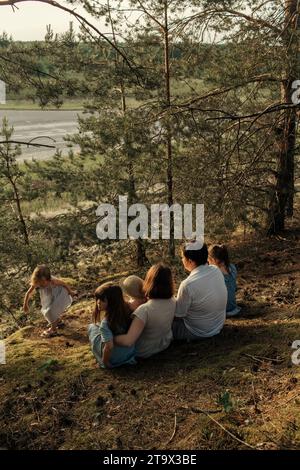 Eine glückliche Familie sitzt auf einem Hügel im Wald und beobachtet den Sonnenuntergang. Familienurlaub. Stockfoto