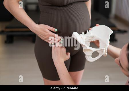 Doula erklärt den Geburtsvorgang an einer Probe des Beckens einer schwangeren Frau. Stockfoto