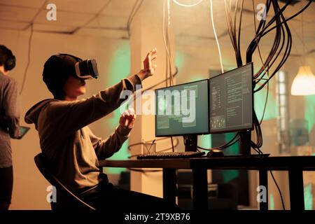 Männlicher Hacker mit vr-Brille, um Computersystem zu hacken, und Pflanzen trojaner Virus für Malware in der Nacht. Junger Erwachsener, der mit 3D Virtual Reality am Headset arbeitet, moderne Technologie-Hacking. Stockfoto