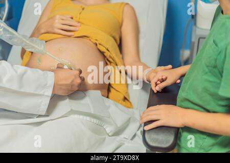 Der Ultraschallbesuch einer schwangeren Mutter teilt die Aufregung mit ihrem Sohn, der sehnsüchtig auf die Ankunft seines kleinen Bruders wartet. Eine herzerwärmende Darstellung Stockfoto