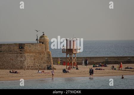 Strandgäste entspannen sich in der Nähe der Mauern der Bastion San Pedro in Cadiz, Spanien. Der öffentliche Strand liegt zwischen zwei alten Burgen an der Bucht. Stockfoto