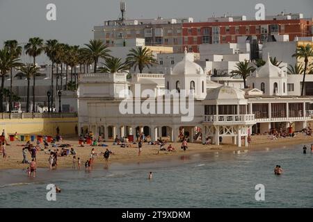 Strandbesucher entspannen sich in der Nähe des Spa of Our Lady of La Palma im maurischen Stil und des echten Gebäudes am Strand von Caleta in Cadiz, Spanien. Der öffentliche Strand liegt zwischen zwei alten Burgen an der Bucht. Stockfoto