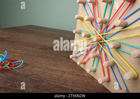 Geoboard aus Holz und Gummibänder auf dem Tisch, Nahaufnahme mit Platz für Text. Motorische Entwicklung Stockfoto