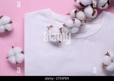 Baumwollzweig mit flauschigen Blumen und weißem T-Shirt auf rosafarbenem Hintergrund, flacher Schnitt Stockfoto