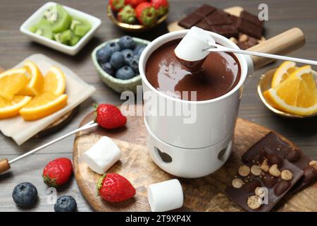 Süßes Marshmallow in Fonduetopf mit geschmolzener Schokolade am Holztisch tauchen Stockfoto