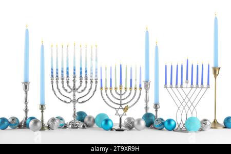 Hanukkah-Feier. Komposition mit verschiedenen Menorahs und festlichen Kugeln auf Tisch vor weißem Hintergrund Stockfoto