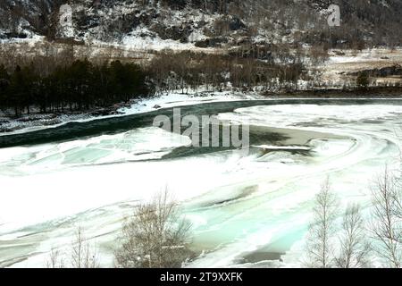 Eine Lichtung auf dem gefrorenen Bett eines wunderschönen Flusses, der an einem Wintermorgen in einem felsigen Bett aus den Bergen fließt. Fluss Katun, Altai, Sibirien, Rus Stockfoto