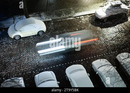 Berlin, Deutschland. November 2023. Ein Auto fährt an geparkten Autos vorbei, die mit Schnee bedeckt sind. Quelle: Sebastian Gollnow/dpa/Alamy Live News Stockfoto