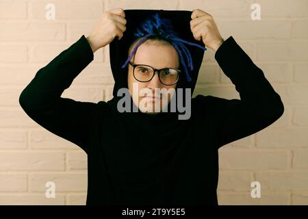 Der lebendige Mann mit markanten lila Dreadlocks und einzigartigem Style zieht eine Kapuze an. Stockfoto