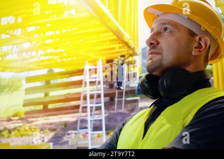 Das Porträt eines jungen Mannes ist ein Ingenieur, der auf der Baustelle mit einem Helm lächelt, der Architekt oder Bauunternehmer steht und die Arme mit Betrügern gekreuzt hat Stockfoto