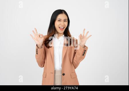 Porträt Happy Asian Woman zeigt OK Handzeichen und blickt auf die Kamera auf weißem isolierten Hintergrund. Stockfoto