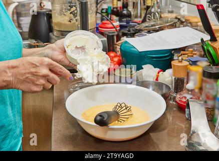 Nahaufnahme der Hände eines Küchenchefs, die gekonnt geschlagene Eier mit Creme Fraiche in einer Edelstahlschale in einer modernen und gut beleuchteten Küche rühren, wobei C gezeigt wird Stockfoto