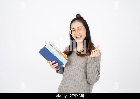 Lächelnder positiver, attraktiver asiatischer junger Frauenfinger mit Mini-Herzzeichen, Porträt von schönen brünetten Haaren mit langen Haaren. Fröhlich, expressio Stockfoto